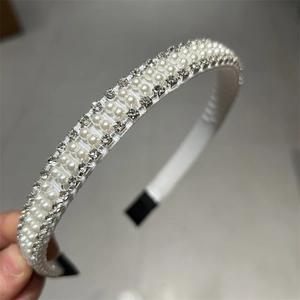 Détail d'un serre-tête en satin blanc avec perles et strass tenu à la main