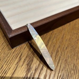 Vue détaillée d'une barrette en acétate avec un fini nacré irisé sur fond de bois