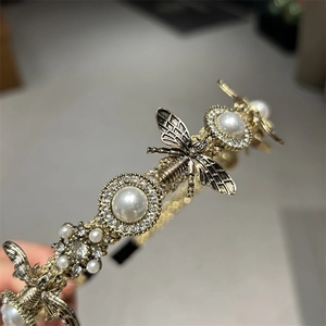 Close-up of golden vintage headband featuring white pearls, crystals and bee motifs
