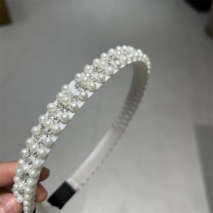 Détail d'un serre-tête avec trois rangées de perles et strass sur tissu blanc