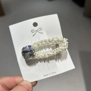 Dettaglio del fermaglio per capelli con perline e strass su cartoncino bianco