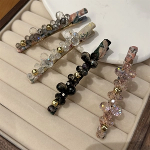 Detail of four crystal beaded hair clips with floral fabric wraps on beige velvet