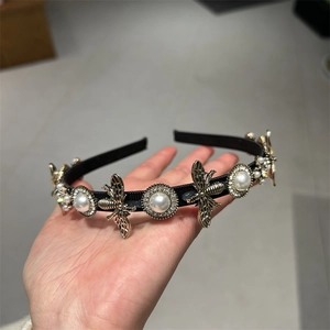 Close-up of a vintage black fabric headband featuring golden bees and pearls with rhinestones