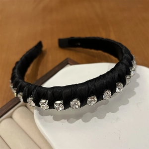 Detail shot of a black satin headband with sparkling rhinestones in a white jewelry box