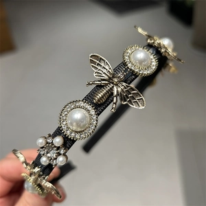 Detailed close-up of retro bee motifs and faux pearls on a black velvet headband