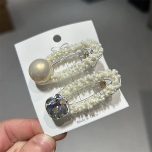 Primo piano di fermagli per capelli con perle tessute e cristalli su carta bianca