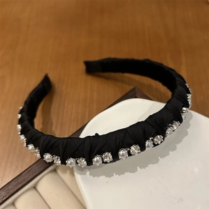 Close-up of black satin headband with pearls and rhinestones on white ceramic tray