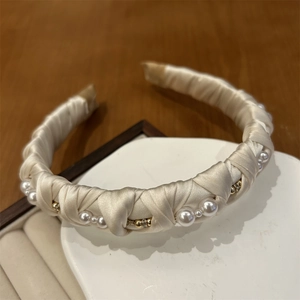 Detailed close-up of champagne satin headband with woven pearls and golden rhinestones