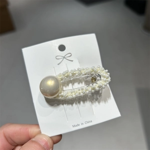 Dettaglio di piccole perle bianche intrecciate attorno a una perla grande su fermaglio