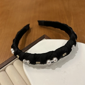 Detail of elegant black satin headband with white pearls and gold beads on a wooden background
