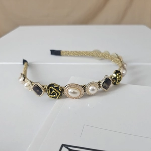 Detail view of woven gold headband with white pearls and black floral resin accents