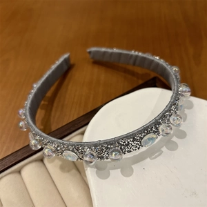 Macro di un cerchietto con strass argentati e perline iridescenti su base in tessuto grigio