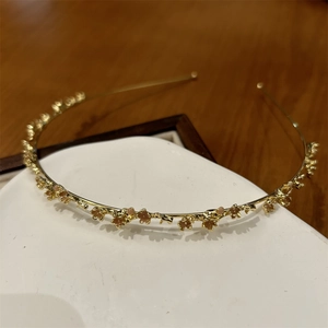 Detail eines dünnen goldenen Blumenstirnbands mit zarten rosa Perlen und Blumendesign