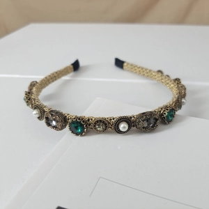 Macro detail of retro golden braided headband with emerald stones and white pearls