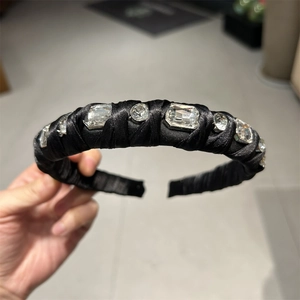 Detailed view of hand-held black satin headband with large sparkling crystal rhinestones