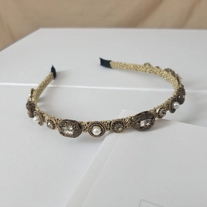 Close-up of gold headband with woven metal patterns, white pearls and grey crystals