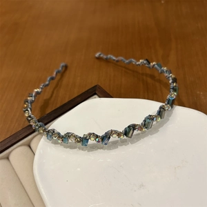 Détail du serre-tête floral ondulé avec cristaux bleus et strass sur un plateau céramique