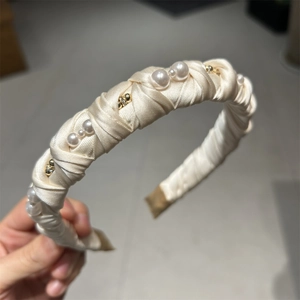 Detailed view of white faux pearls and gold beads on a woven satin ribbon headband