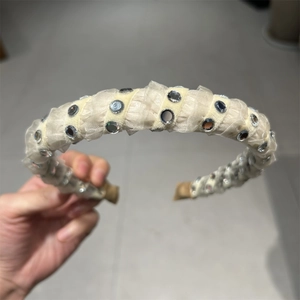 Close-up of cream pleated fabric headband with shiny silver rhinestones detailing