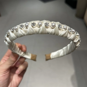Close-up of cream fabric headband featuring woven texture with inlaid pearls and rhinestones