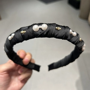 Detailed view of black satin headband with white faux pearls and gold beads on a soft band