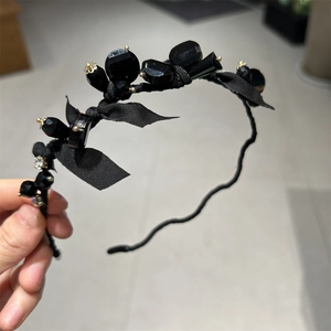 Close-up of black fabric headband featuring elegant ribbon bow, crystals and beads