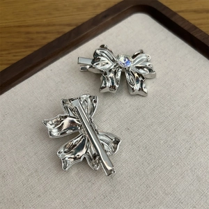 Silver metal bow hair clips with radiant gemstone on a minimalist fabric display