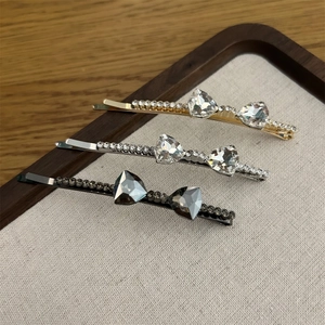 Detail view of crystal bow hair clips in gold, silver, and black on a linen tray