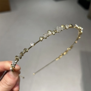 Detailansicht eines goldfarbenen Haarreifens mit Herzmotiven, Zirkonia und Perlen