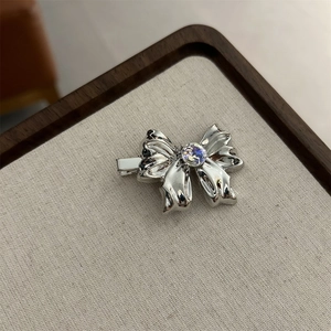 Polished silver metal bow hair clip with central zircon on a textured display stand