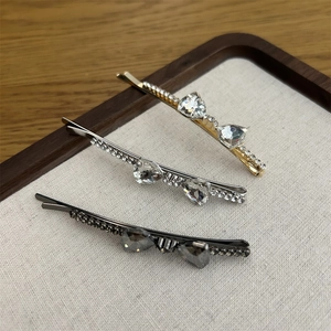 Three crystal bow hair clips in gold, silver and gray displayed on a beige tray