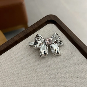 Polished silver metal bow hair clip with pink rhinestone center on textured background