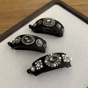 Three elegant black velvet banana hair clips with pearls and rhinestones on a wooden tray
