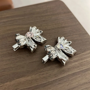 Detail of silver bow hair clips with pink and clear gemstones on a wooden board
