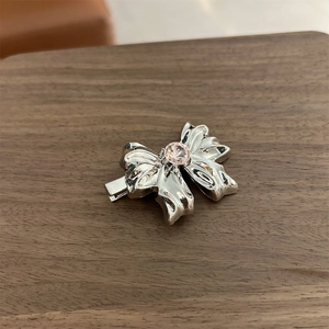 Close-up of a silver bow hair clip with a pink rhinestone on a dark wooden surface