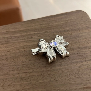 Close-up of a silver bow hair clip with a sparkling central crystal on dark wood background