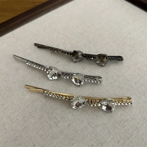 Detailed view of three crystal bow hair clips in gold, silver, and gunmetal finishes