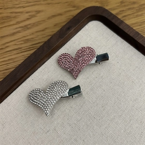 Detail von rosa und silbernen herzförmigen Haarspangen mit Strass auf Leinentablett