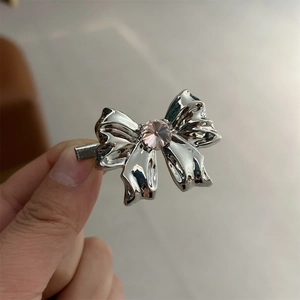 Detail of silver bow hair clip featuring a centered pink rhinestone on metal surface