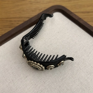 Detail view of a luxury black banana clip with rhinestones and a grey crystal stone