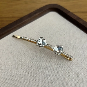 Elegant gold crystal bow hair clip with sparkling rhinestones on a textured display
