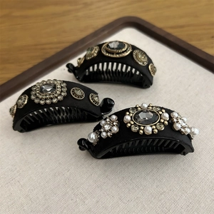 Detailed view of matte black banana clips with pearls and grey rhinestones on fabric