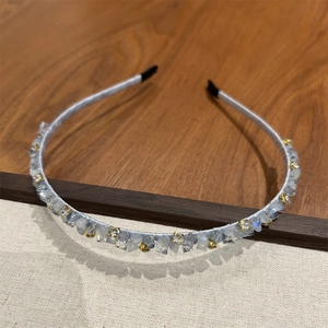 Détail de cristaux bleu clair et perles dorées sur un bandeau en satin gris