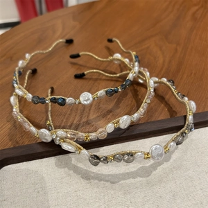 Detailed shot of two gold wavy headbands with crystals and faux pearls on a wood surface