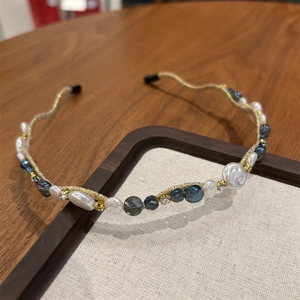 Detail of slim gold headband featuring white pearls and blue crystal accents on wood