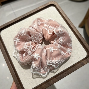 Gros plan d'un chouchou en satin rose avec broderie de dentelle blanche sur plateau bois