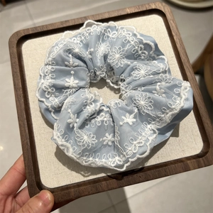 Détail d'un chouchou en satin bleu clair avec broderie florale en dentelle blanche