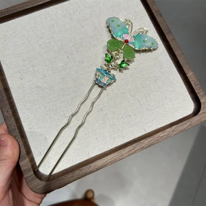 Detail of a vintage U-shaped hair fork featuring a green enamel butterfly and floral basket