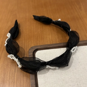 Detail of black organza headband with delicate white pearl clusters on wooden surface