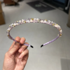 Détail du serre-tête en tissu lilas orné de strass, cristaux et perles dorées